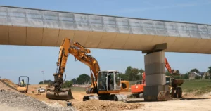 Engins de chantier en action sous un pont moderne en béton, lors de travaux de terrassement sur une route en construction.
