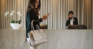 Femme souriante avec valise et téléphone à la réception d’un hôtel