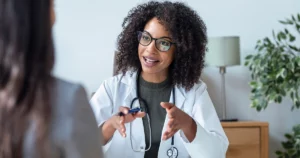 Une médecin libérale en blouse blanche échange avec une patiente dans son cabinet