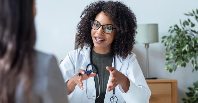 Une médecin libérale en blouse blanche échange avec une patiente dans son cabinet