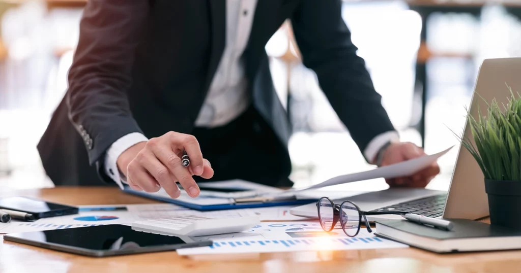 Expert-comptable analysant des documents financiers sur un bureau avec graphiques et ordinateur portable
