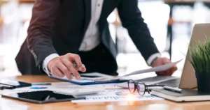 Expert-comptable analysant des documents financiers sur un bureau avec graphiques et ordinateur portable