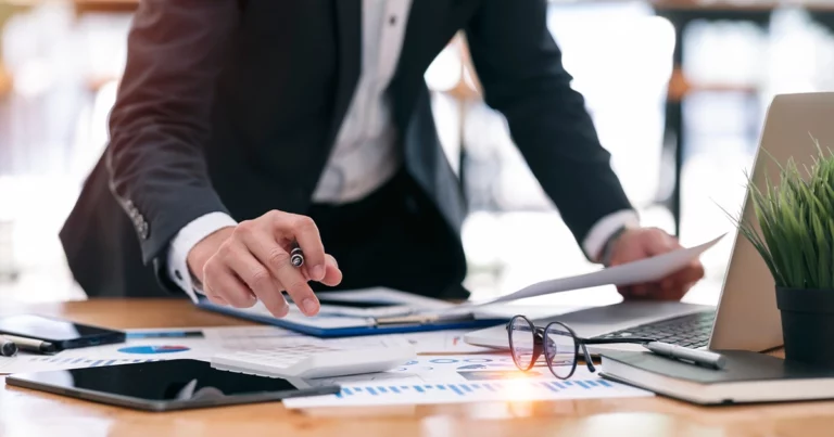 Expert-comptable analysant des documents financiers sur un bureau avec graphiques et ordinateur portable